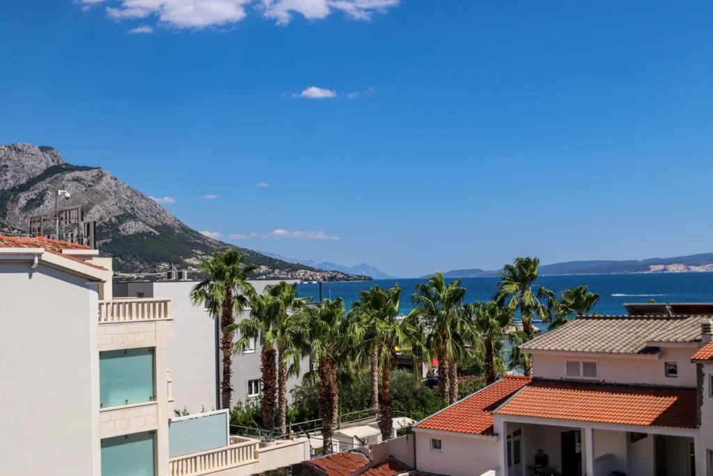 Häuser und Palmen an einer Küste mit Meer und Bergen im Hintergrund